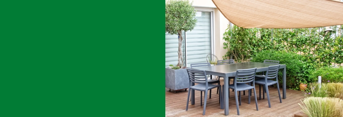 Graue Sitzgruppe unter einem Sonnensegel auf einer Holzterrasse mit vielen Pflanzen.